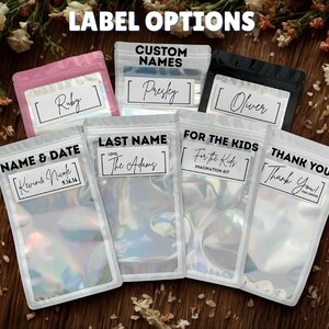 May include: An assortment of clear, iridescent pouches with various label options. Labels include names like "Ruby," "Presley," and "Oliver," along with phrases such as "Name & Date," "Last Name," "For the Kids," and "Thank You." The text "Label Options" is at the top.