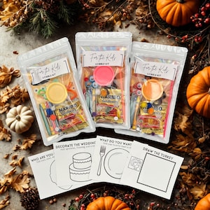 May include: Three clear plastic bags labeled "For the Kids" and "Gobble Kit" filled with craft supplies and candy. The bags are surrounded by pumpkins, gourds, and fall foliage. Coloring pages are also visible.