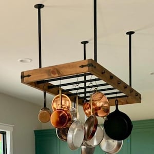 Puede incluir: Un estante de madera para ollas con tuberías y ganchos de metal negro que cuelgan del techo. El estante está lleno de varias ollas y sartenes de cobre y acero inoxidable.