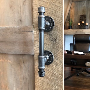 May include: Black industrial pipe door handle with a black metal flange. The handle is mounted on a wooden door.