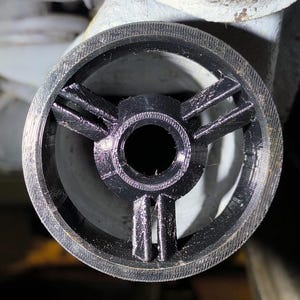 May include: Close-up of a black, circular automotive part with a central hole and three radiating arms. The part has a textured outer ring and appears to be made of a durable material. The background is dark and out of focus.