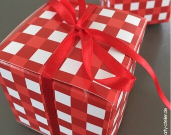 Pode incluir: Uma caixa de presente vermelha e branca quadriculada com uma fita de cetim vermelha amarrada em um laço. A caixa está sobre uma superfície cinza.