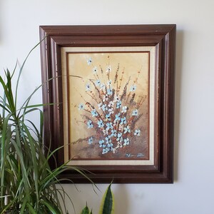 May include: A framed painting of a bouquet of blue and white flowers with a brown background. The painting is signed "William Patti" in the bottom right corner.