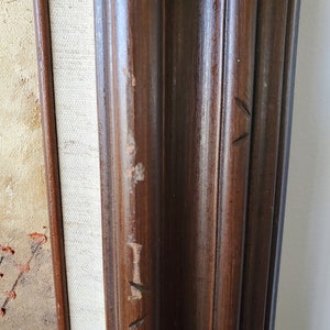 May include: Close-up of a dark brown wooden frame with visible wood grain and a few small scratches. The frame is likely for a painting or artwork.