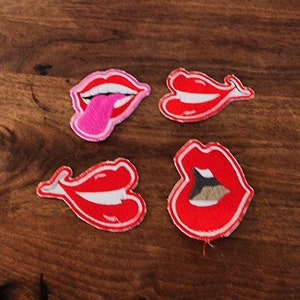 May include: Four red and pink felt patches shaped like lips with white outlines. Two of the patches have a white line inside the lips, and one has a pink tongue sticking out.