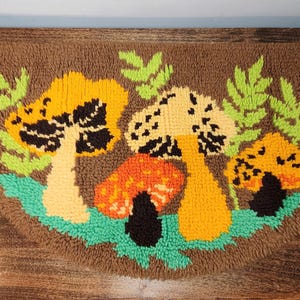 May include: A half-circle rug with a brown background and a colorful mushroom design. The mushrooms are yellow, orange, and cream with black details, set against green leaves and a turquoise base. The rug is made of a textured material.