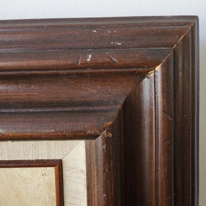 May include: Close-up of the top corner of a dark brown wooden picture frame. The frame has a simple, slightly raised molding design.