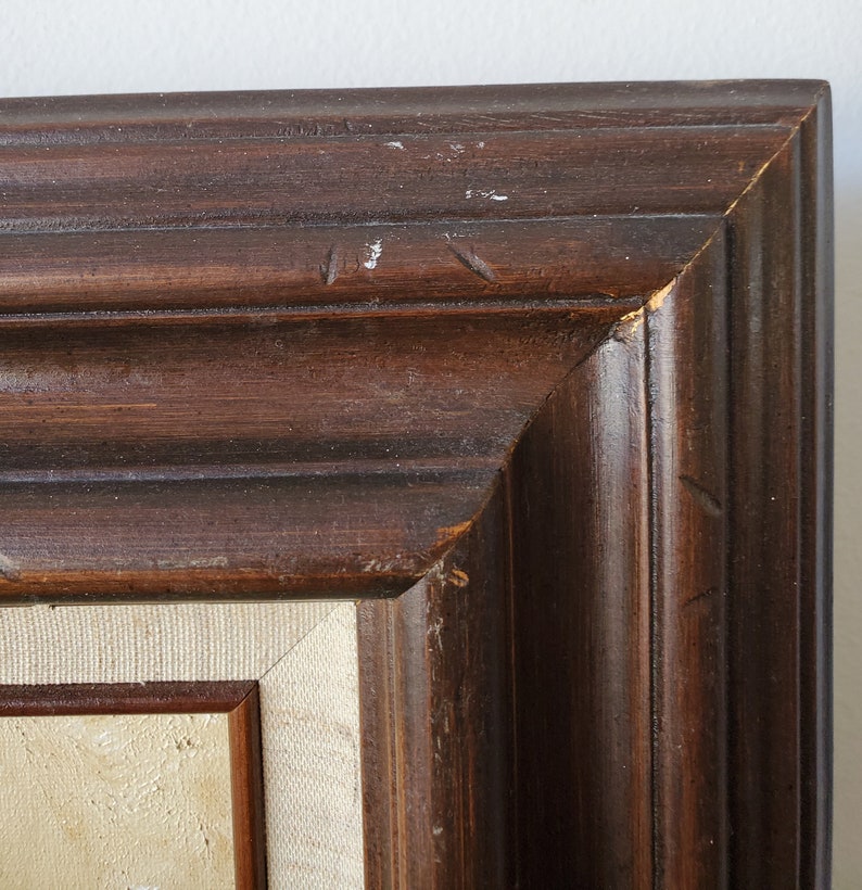 May include: Close-up of the top corner of a dark brown wooden picture frame. The frame has a simple, slightly raised molding design.