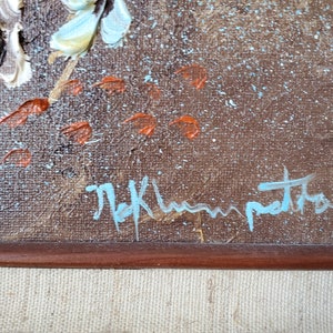 May include: Close-up of a brown canvas with a blue signature that reads "M.K. Hampton". The canvas has a textured surface with white and orange paint splatters.