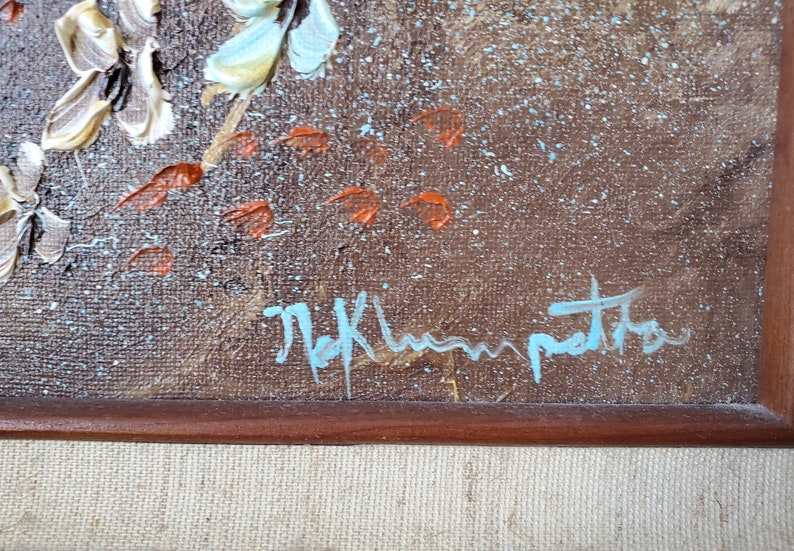May include: Close-up of a brown canvas with a blue signature that reads "M.K. Hampton". The canvas has a textured surface with white and orange paint splatters.