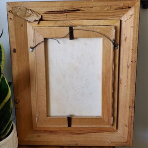 May include: A wooden picture frame with a white canvas inside. The frame has a brown stain and is slightly distressed. The back of the frame has a label that reads "Made in Taiwan".