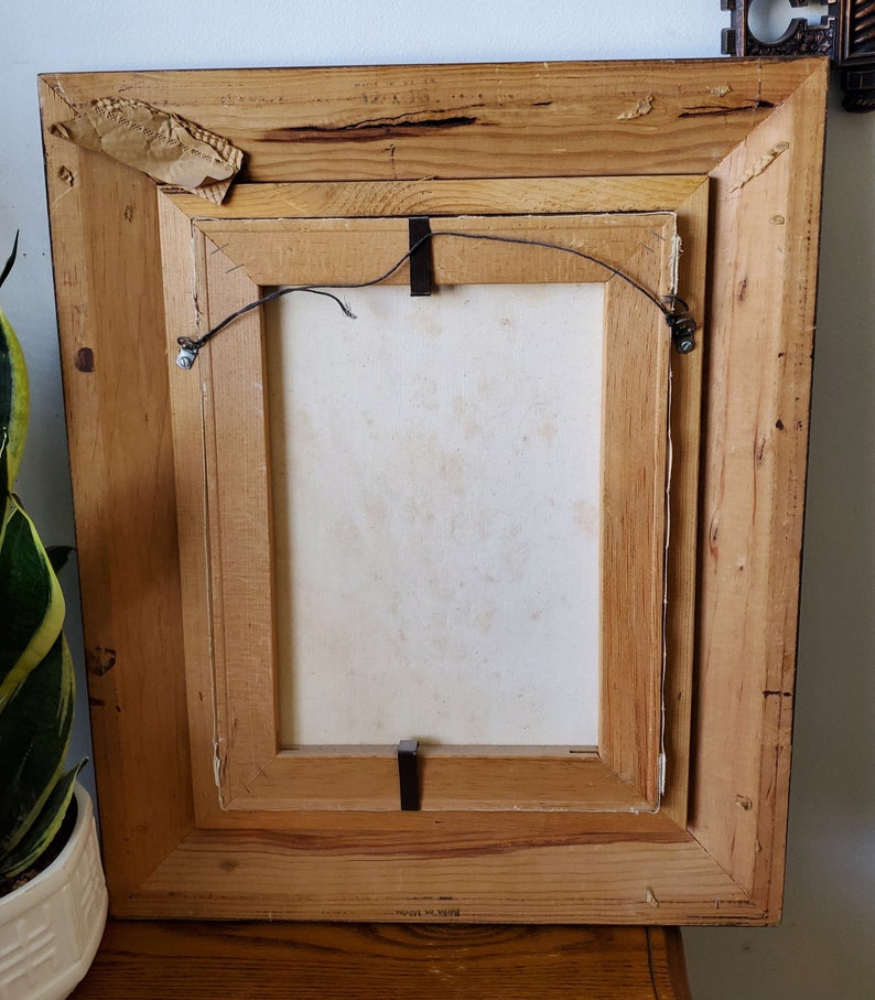 May include: A wooden picture frame with a white canvas inside. The frame has a brown stain and is slightly distressed. The back of the frame has a label that reads "Made in Taiwan".