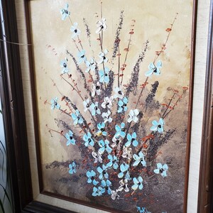 May include: A framed painting of a bouquet of blue and white flowers with brown stems and leaves on a beige background. The painting is signed "Thelma Pettit" in the lower right corner.