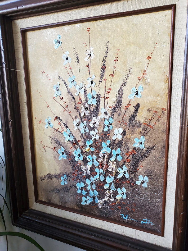 May include: A framed painting of a bouquet of blue and white flowers with brown stems and leaves on a beige background. The painting is signed "Thelma Pettit" in the lower right corner.