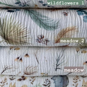 May include: Four different fabric swatches with various nature-inspired prints. The top swatch features a white background with small, colorful wildflowers. The second swatch has a white background with green and brown leafy patterns. The third swatch has a white background with small brown and white floral patterns. The bottom swatch has a white background with small brown and green floral patterns and a small brown squirrel and a gray hedgehog.