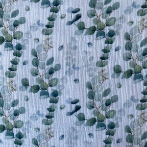 May include: White fabric with a repeating pattern of green eucalyptus leaves and white flowers.