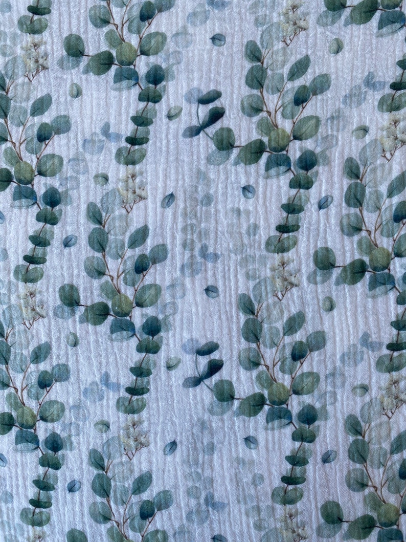 May include: White fabric with a repeating pattern of green eucalyptus leaves and white flowers.