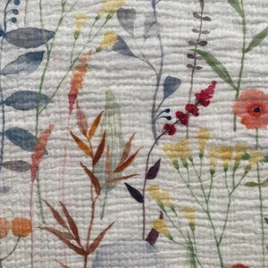 May include: Close-up of a white fabric with a floral pattern. The design features watercolour-style illustrations of various wildflowers in shades of red, yellow, orange, blue, and green. The fabric has a textured, crinkled appearance.