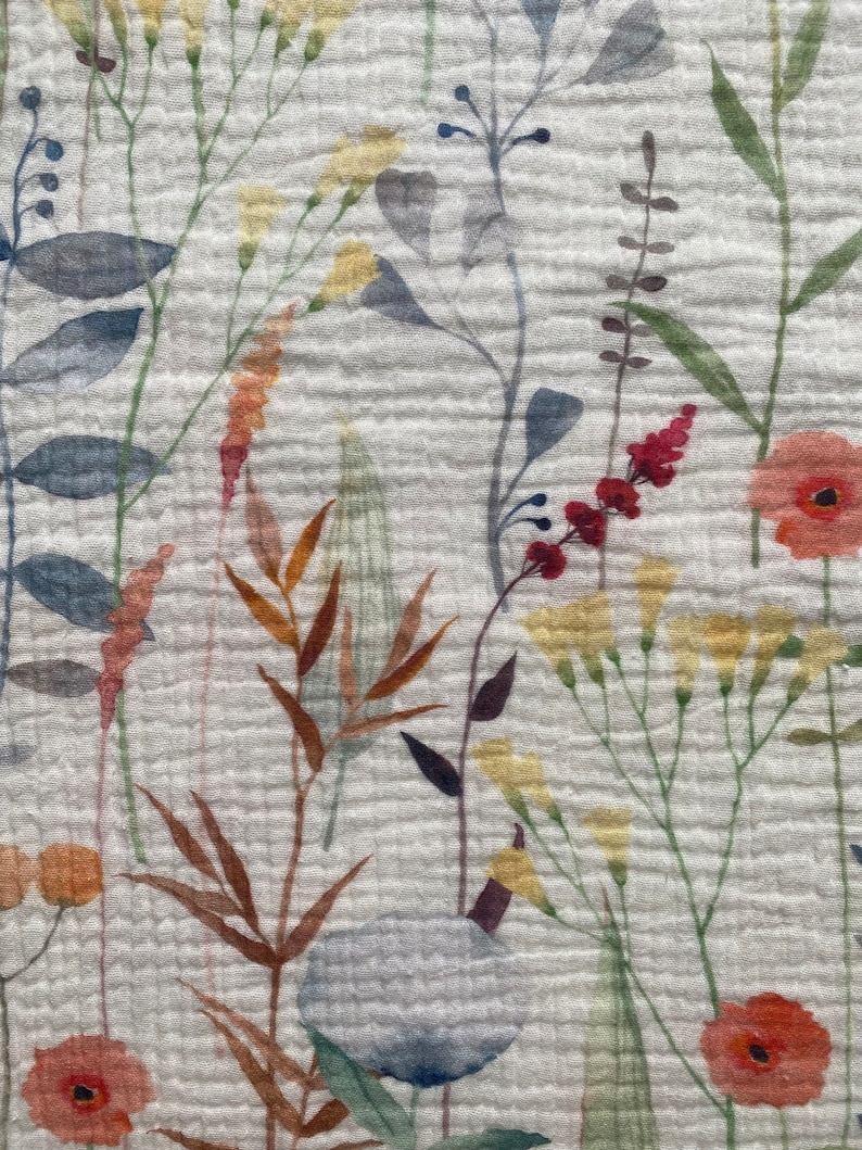 May include: Close-up of a white fabric with a floral pattern. The design features watercolour-style illustrations of various wildflowers in shades of red, yellow, orange, blue, and green. The fabric has a textured, crinkled appearance.