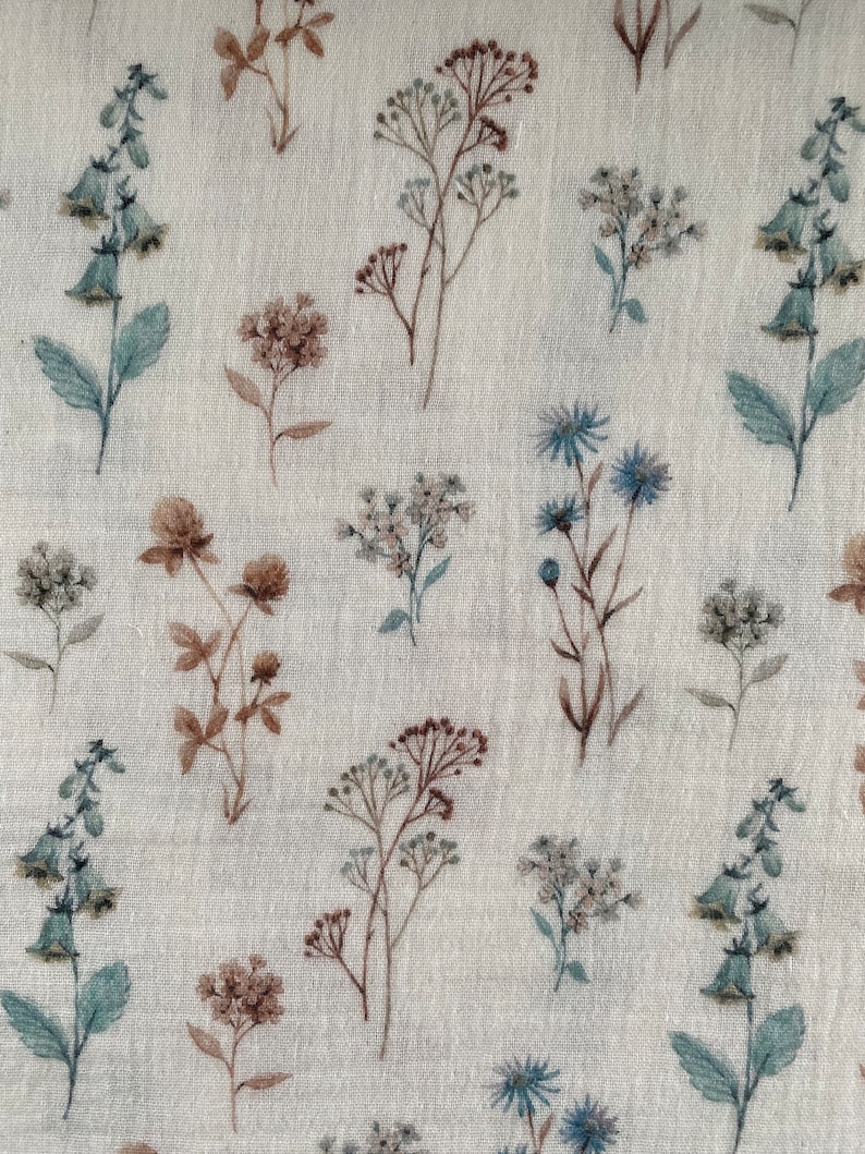 May include: A beige fabric with a repeating pattern of various floral designs in shades of brown, blue, and green. The flowers are stylized and resemble wildflowers.
