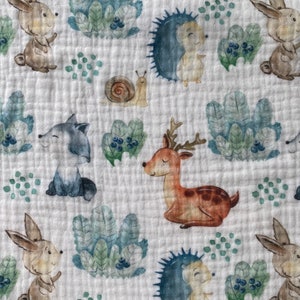 May include: A white fabric with a repeating pattern of woodland animals, including deer, rabbits, hedgehogs, and snails. The animals are drawn in a watercolor style with muted colors.