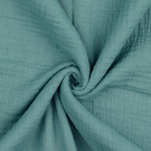 May include: A close-up of a soft, teal-colored fabric with a crinkled texture. The fabric is folded and draped, creating a swirling pattern.