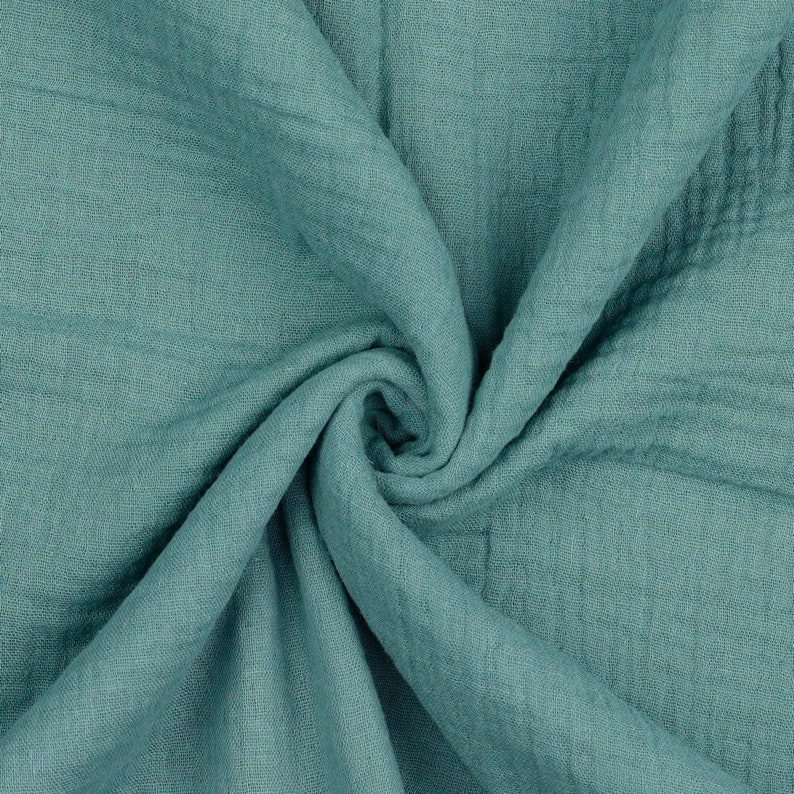 May include: A close-up of a soft, teal-colored fabric with a crinkled texture. The fabric is folded and draped, creating a swirling pattern.