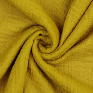 May include: A close-up of a soft, yellow fabric with a textured surface. The fabric is folded and draped, creating a swirling pattern.