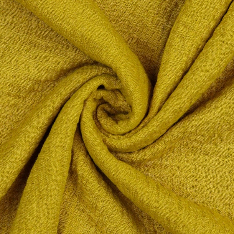 May include: A close-up of a soft, yellow fabric with a textured surface. The fabric is folded and draped, creating a swirling pattern.