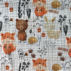 May include: A white fabric with a repeating pattern of brown bears, orange foxes, white rabbits, brown birds, and snails. The background is white with a subtle texture.