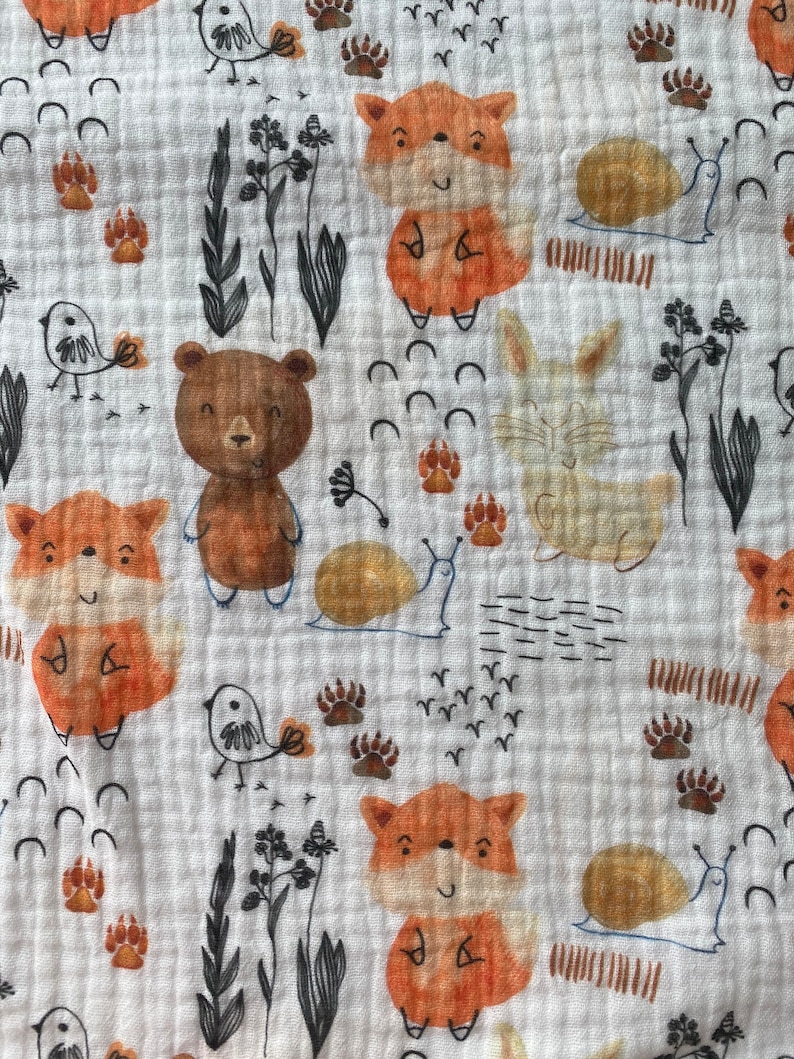 May include: A white fabric with a repeating pattern of brown bears, orange foxes, white rabbits, brown birds, and snails. The background is white with a subtle texture.