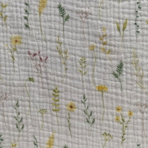 May include: White fabric with a floral design. The pattern includes watercolour-style illustrations of wildflowers in yellow, green, and pale pink. The fabric has a textured, quilted appearance.