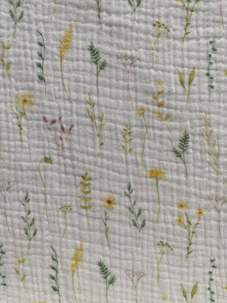 May include: White fabric with a floral design. The pattern includes watercolour-style illustrations of wildflowers in yellow, green, and pale pink. The fabric has a textured, quilted appearance.