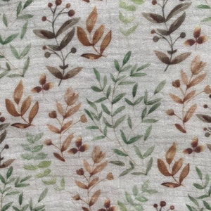 May include: Close-up of a fabric with a repeating pattern of watercolour-style botanical elements. The design features brown, green, and tan leaves and berries on a light grey background. The fabric has a slightly textured appearance.