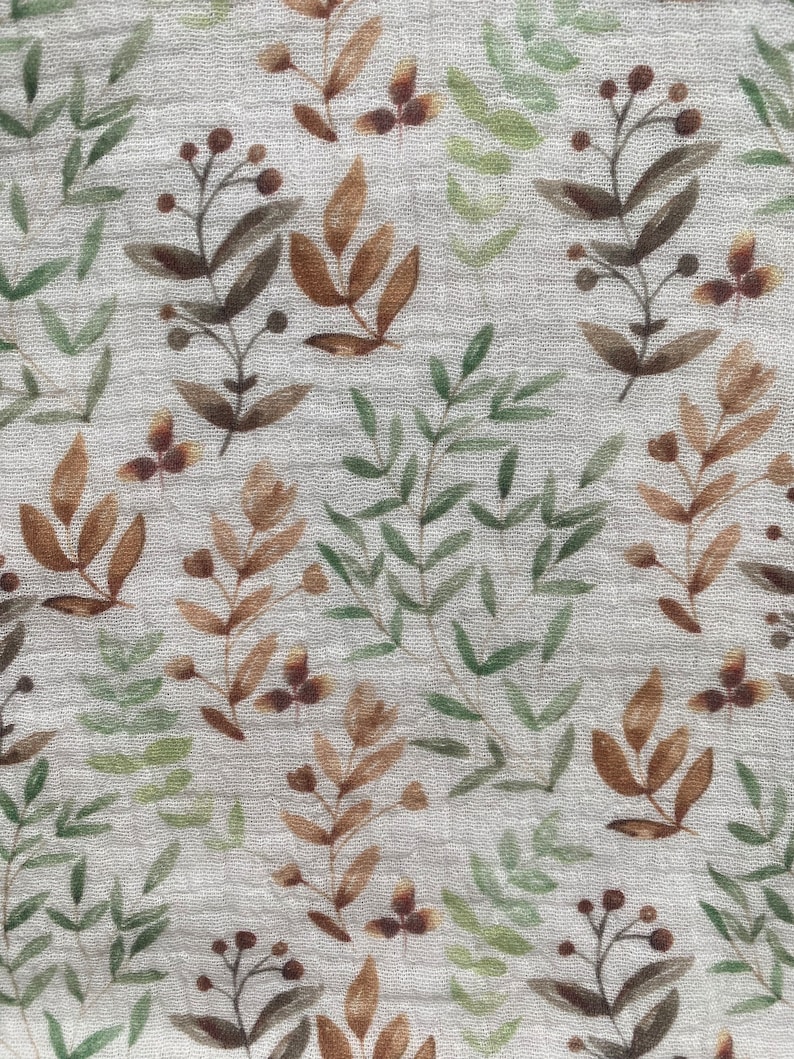 May include: Close-up of a fabric with a repeating pattern of watercolour-style botanical elements. The design features brown, green, and tan leaves and berries on a light grey background. The fabric has a slightly textured appearance.