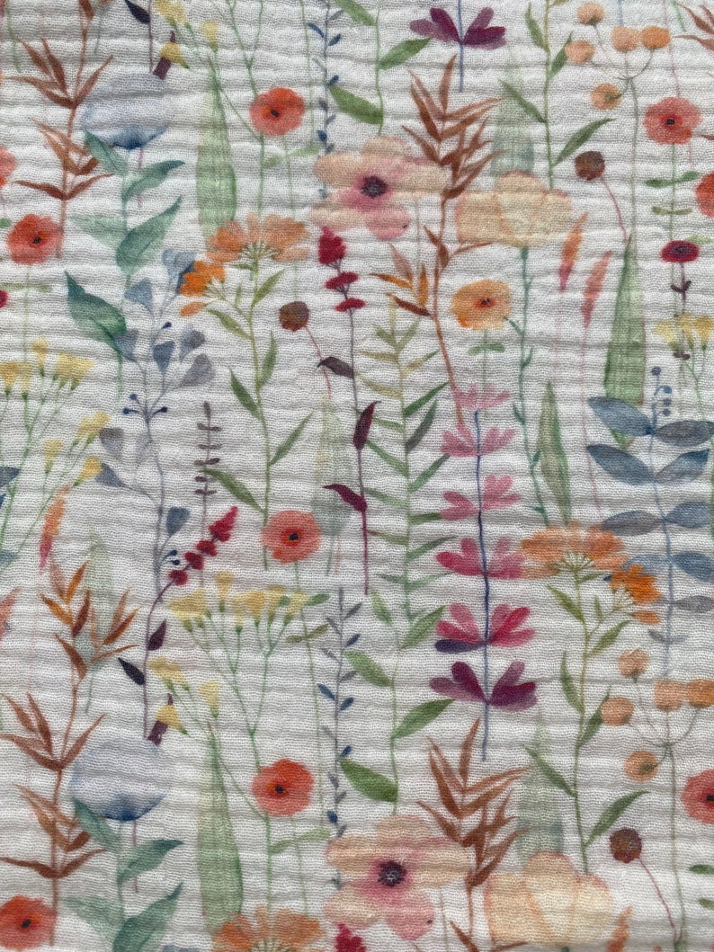 May include: Close-up of a white fabric with a watercolour floral pattern. The design features a variety of flowers in shades of orange, pink, red, and purple, along with green leaves and brown stems. The fabric has a textured, crinkled appearance.