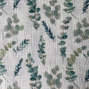 May include: White fabric with a repeating pattern of green eucalyptus leaves. The leaves are watercolor-style and have a slightly faded look.