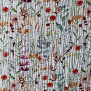 May include: White fabric with a floral pattern featuring various shades of red, orange, yellow, and green. The flowers are stylized and resemble watercolor paintings.