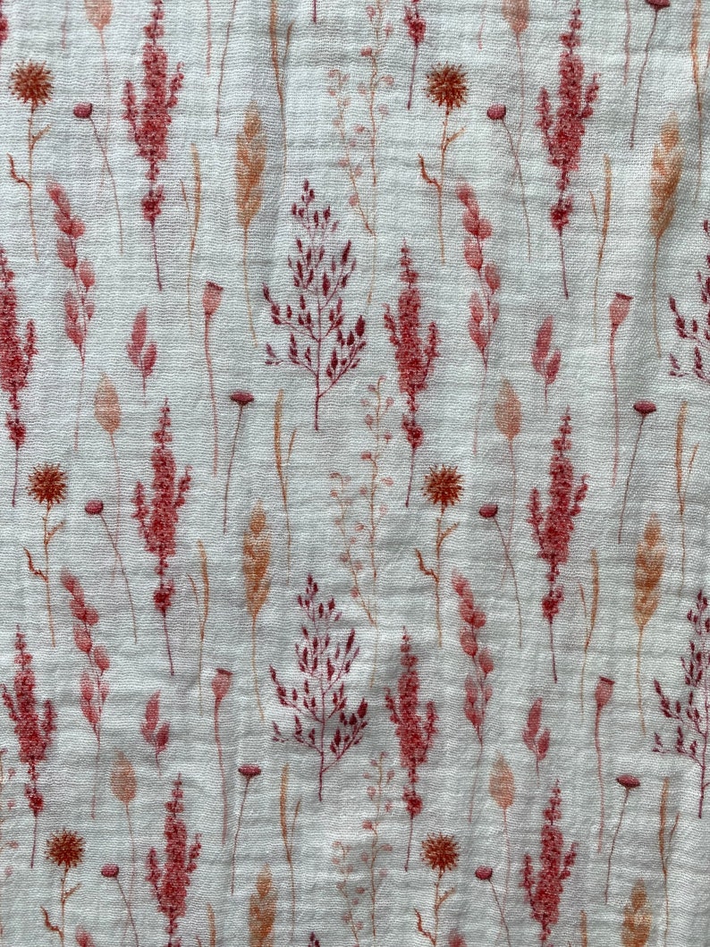 May include: A white fabric with a repeating pattern of pink and brown pressed flowers. The flowers are various types of grasses and wildflowers.