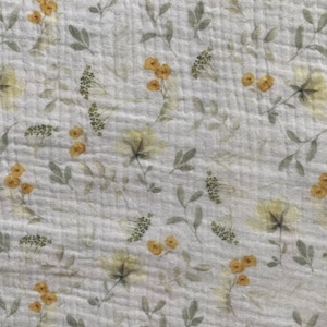 May include: A light grey fabric with a delicate floral pattern. The design features yellow and green flowers and leaves scattered across the surface. The fabric has a slightly textured appearance.