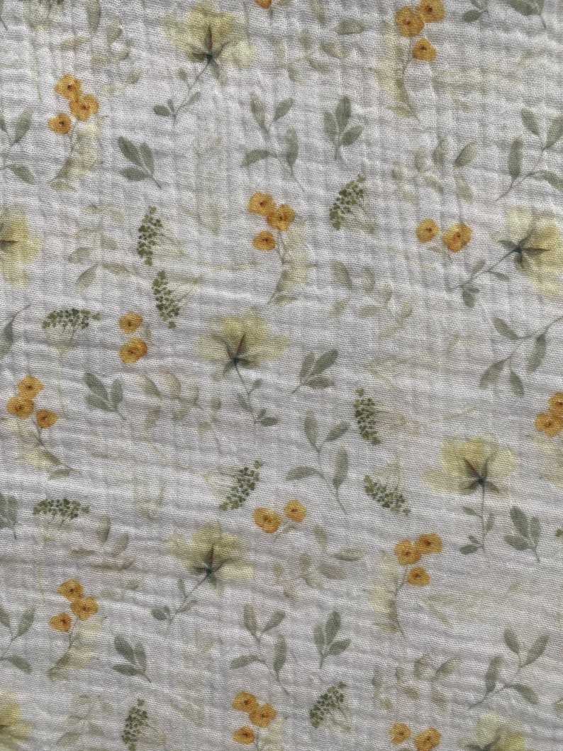 May include: A light grey fabric with a delicate floral pattern. The design features yellow and green flowers and leaves scattered across the surface. The fabric has a slightly textured appearance.