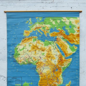 Könnte beinhalten: Eine Vintage-Karte von Afrika, die an einer Wand hängt. Die Karte zeigt detaillierte geografische Informationen, einschließlich Länder, Städte und Gelände. Die Karte ist auf blauem Hintergrund gedruckt und mit Holzstäben versehen.