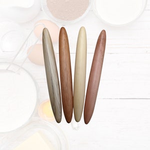 May include: Four wooden rolling pins of different colours and wood grains. The rolling pins are arranged vertically, with the lightest coloured rolling pin on the left and the darkest coloured rolling pin on the right.