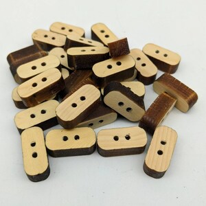 May include: A pile of wooden buttons with two holes each. The buttons are a light brown colour with a darker brown border.