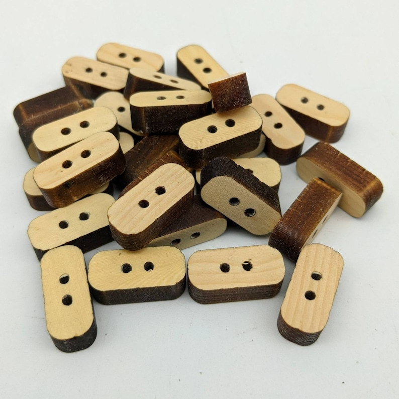 May include: A pile of wooden buttons with two holes each. The buttons are a light brown colour with a darker brown border.