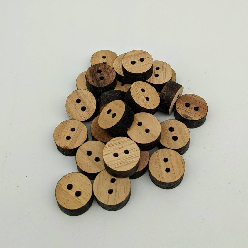 May include: A pile of wooden buttons with two holes each. The buttons are a light brown colour with a darker brown edge.