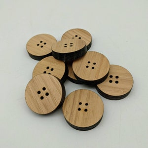 May include: A group of eight wooden buttons with a dark brown edge and five holes in the centre. The buttons are arranged in a pile on a white surface.