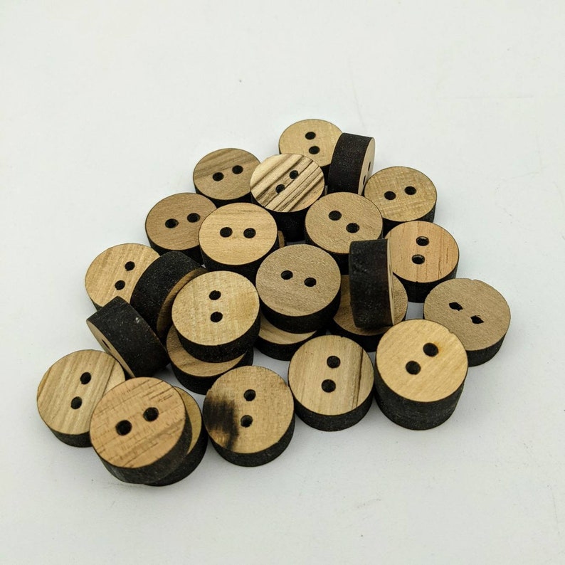 May include: A pile of wooden buttons with two holes each. The buttons are a light brown colour with dark brown edges.