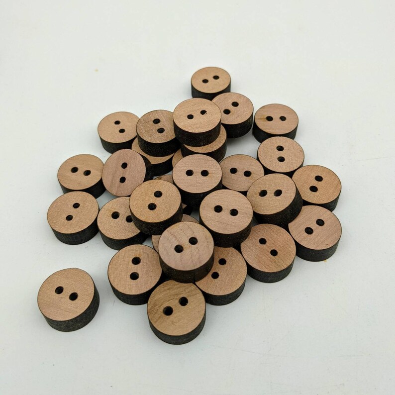 May include: A pile of wooden buttons with two holes each. The buttons are a light brown colour with a dark brown edge.