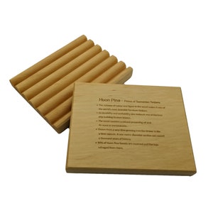 May include: A wooden soap dish with a grooved design and a small wooden block with text about Huon Pine, a type of wood native to Tasmania. The text describes the wood's unique qualities, including its durability, workability, and distinctive scent. It also mentions that the wood is slow-growing and that 80% of Huon Pine forests are reserved.